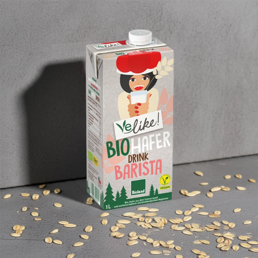 Velike! Bio Hafer Drink Barista – 1-Liter-Packung auf grauem Untergrund, umgeben von Haferkörnern. Pflanzliche Milchalternative aus regionalem Bio-Hafer, ideal zum Aufschäumen für Kaffee.